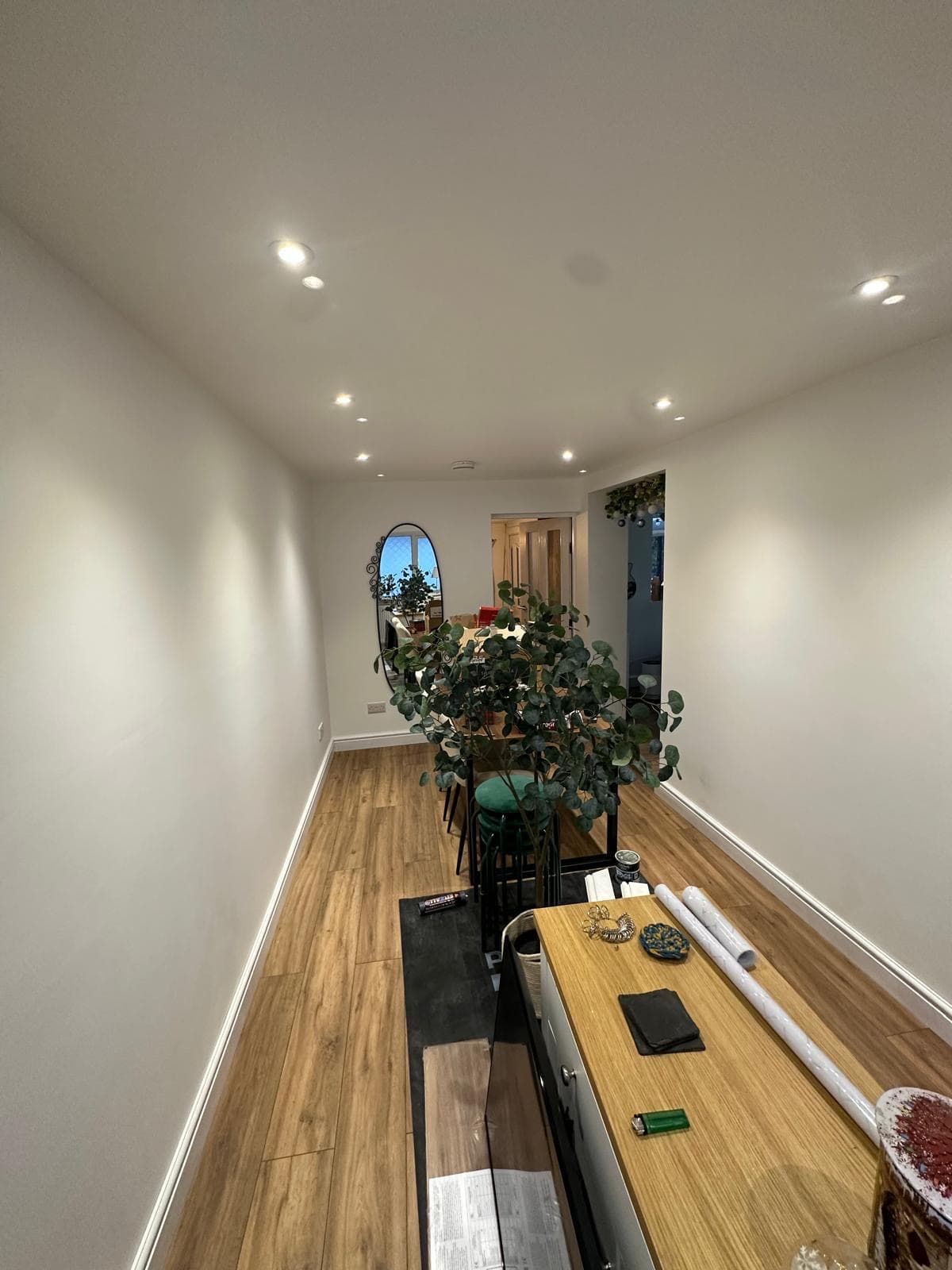 A finished garage conversion used as a dining room, with downlights, wood-effect flooring and a long table, looking through to the hallway